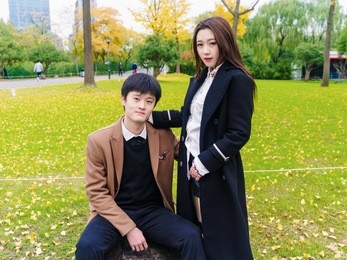portrait of couple of chinese young people sit in autumn park, girl put her hand on boyfriend's shoulder, lover concept.