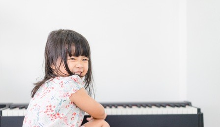 beautiful little asian girl playing piano in living room or music school.kindergarten child having fun with learning to play music instrument.education, skills concept.