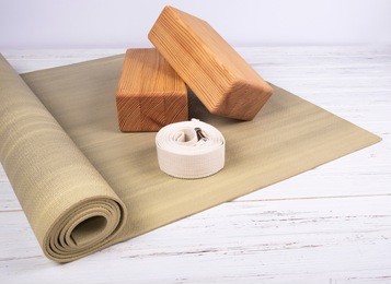 green yoga mat, two wooden blocks and white belt on white wooden  background. yoga practice, relaxation and meditation concept.