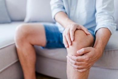 man suffering from knee pain sitting sofa. a mature man massaging his painful knee. man suffering from knee pain at home, closeup. pain knee 