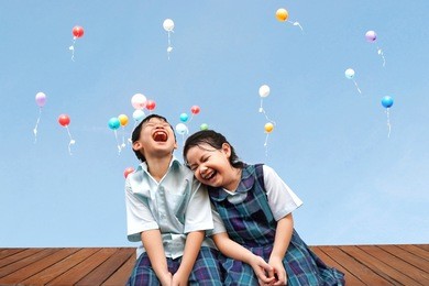 funny asian little kids brother and sister sitting on the wooden terrace with colourful balloons background.laughing and happiness of cute kid in uniform school,education,family,children concept.