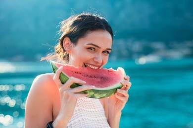 attractive young woman on the beach eating watermelon