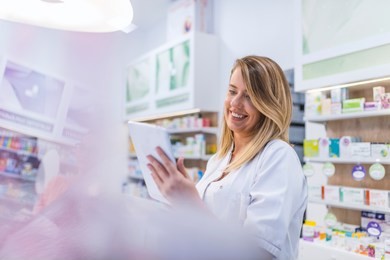 pharmacist working with a tablet computer in the pharmacy holding it in her hand while reading information. cheerful happy pharmacist chemist woman working in pharmacy drugstore with tablet computer