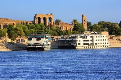 egypt. cruise ships docked at kom ombo on the nile. the temple of sobek and haroeris in background - seen colonnade of the hypostyle hall