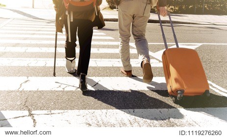 woman wearing ankle support travelling together with man pulling orange baggage