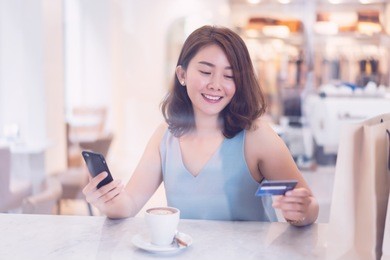 asian thai elegant brown girl in blouse in cafe holding mobile phone and credit-card signing up on a website application. businesswoman paying with a credit card while shopping online by smartphone