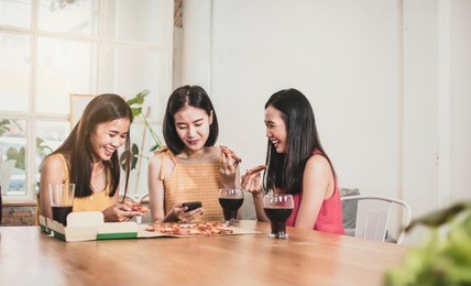 group of asian funny women enjoying eating pizza and playing phone at home