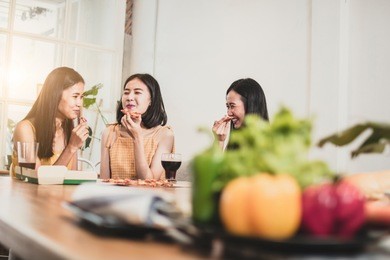 group of thai asian funny women enjoying eating pizza and playing phone at home and don't care fruits on table
