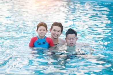 father and his two son play in clear water swimming pool - happy family play time concept
