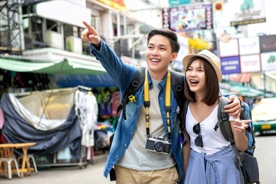 young happy asian couple tourist backpackers enjoy traveling in khao san road during vacations in bangkok, thailand