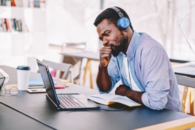 young african american hipster guy in headphones watching online football match worried and nervous about team, african american hipster guy concentrated on training webinar learning online course