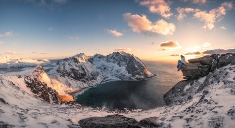 panorama of mountaineer sitting on rock on peak mountain of arctic coastline at sunset. ryten mountain, lofoten islands, norway