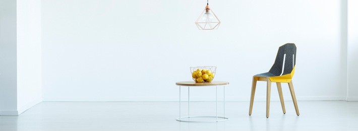 lamp above table with citruses next to yellow chair in white interior with copy space. real photo with a place for your chair