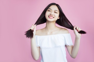 a happy asian woman is very satisfied with her appearance. young and healthy, healthy hair and skin. cheer and crimson on a pink background. enjoy life and smile, friendly, sweet and beautiful