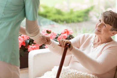 doctor helping an elderly woman with parkinson's disease get up from a sofa in a rehabilitation facility