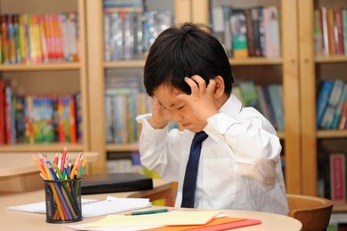 frustrated asian schoolboy in school uniform ( white shirt and tie ) doing homework