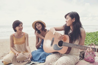 younger asian woman friend vacation relaxing playing guitar and sing a song on sea beach