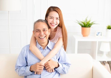 happy asian daughter holding father on sofa