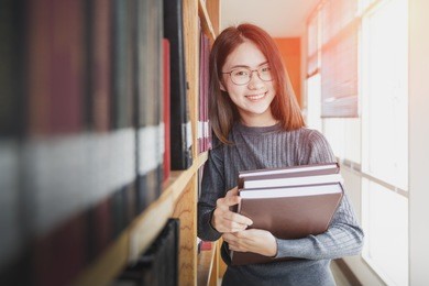 back to school education knowledge college university concept, beautiful female college student holding her books smiling happily standing in library, learning and education concept