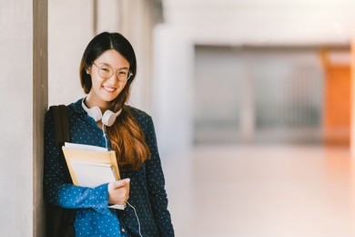 young beautiful asian high school girl or college student wearing eyeglasses, smiling in university campus with copy space. education, casual lifestyle, geek or nerd smart people concept