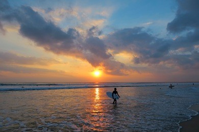 young surfer silhouette with surfboard at beautiful sunset background, kuta beach, bali, indonesia