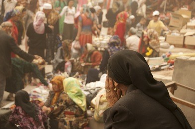 old woman sat staring at people shopping at a market in kashgar, china
