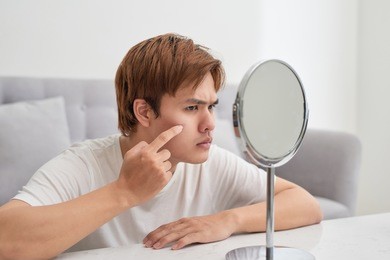 handsome man looking at himself in mirror. squeezing pimple.