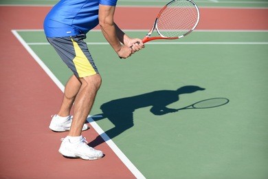 tennis player holding racket casting shadow on court