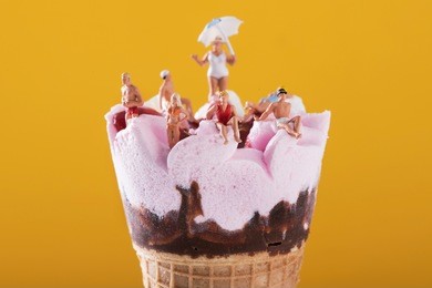 closeup of some miniature people wearing swimsuit relaxing on a pre-filled ice cream cone, against an orange background