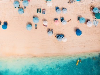 top view of sandy beach with turquoise sea water and colorful blue umbrellas, aerial drone shot