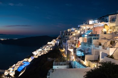 whitewashed houses with view onto sea and oia during sunset in imerovigli, santorini, greece