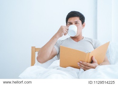 asian male is reading book and drink coffee on morning bed