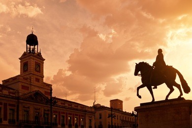 sunset in puerta del sol, madrid with casa de correos at the left and the equestrian statue of carlos iii at the right