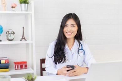 asian female doctor work at hospital office desk giving patient convenience online service advice, smiling write a prescription order medical with smartphone, health care, preventing disease concept.