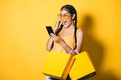 beautiful young woman with shopping bags using her smart phone on yellow background.shopaholic shopping fashion.
