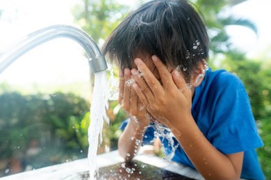 young asian boy wash his face by a water from modern faucet in a garden