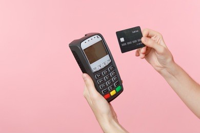 close up cropped photo of female holding in hands wireless modern bank payment terminal to process and acquire credit card payments, black card isolated on pink background. copy space for advertising