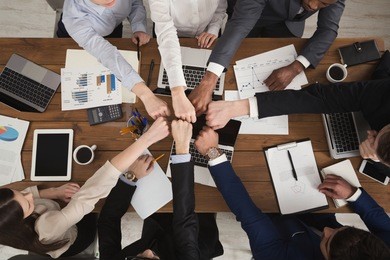young people putting their fists together as symbol of unity and achievement, top view. group of people fist bump assemble together over workplace. teamwork concept, copy space in middle