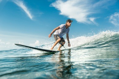 young male surfer riding waves in ocean at nusa dua beach, bali, indonesia