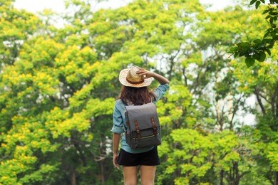 woman traveler with backpack holding hat and looking at the view in forest, travel concept