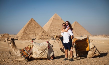 young couple taking posing for a photo in front of camels with the great pyramids of giza in the background