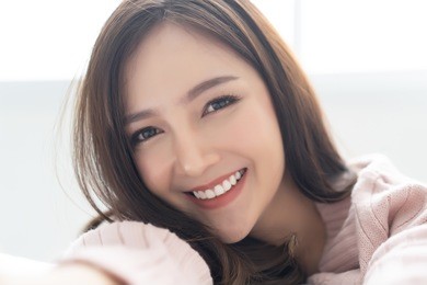 closeup portrait of inspired caucasian asian lady wearing knitted sweater pink cold smilling and taking selfie at her home.concept woman lifestyle and winter. autumn, winter season.