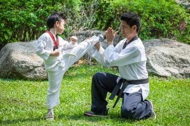 father coach is training his son boy taekwondo kick in green park .children kid and teacher master trainer are learning karate outdoor in the nature park