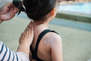 mom applying sunscreen on little girl back before swim
