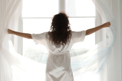 morning of beautiful young woman opening curtains in bedroom