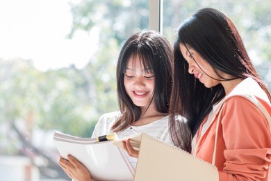 two young girls asian college groups of students using tablet, laptop to studying together with documents paper for report in classroom. serious study for school assignment, education concept