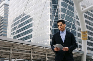 young handsome asian business man standing and working about finance on digital tablet in office building, technology, internet, investment, stock market and global business concept