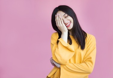 pretty girl cute laughs in a frame on a pink background. laughter, joy, mercy, youth, good joke, emotional reaction, hand covers the face, funny and friendly, sincerity