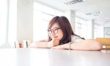 young female student is smiling with empty copy space on desk in library in campus of university