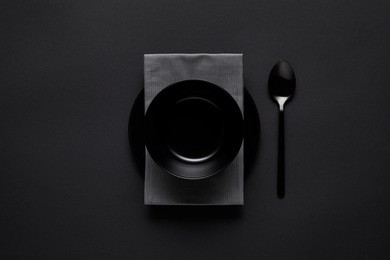 top view of black bowl, spoon, kitchen towel and plate on black table, minimalistic concept